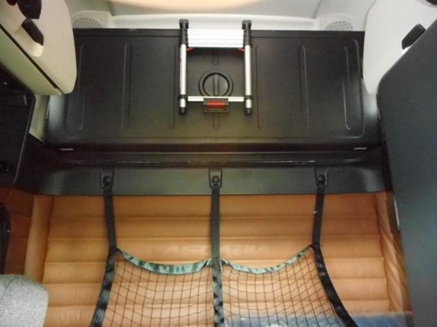 Freightliner Cascadia 126 cab interior showing storage compartment and wooden floor, with straps securing a mesh net and a black under-bunk storage tray.