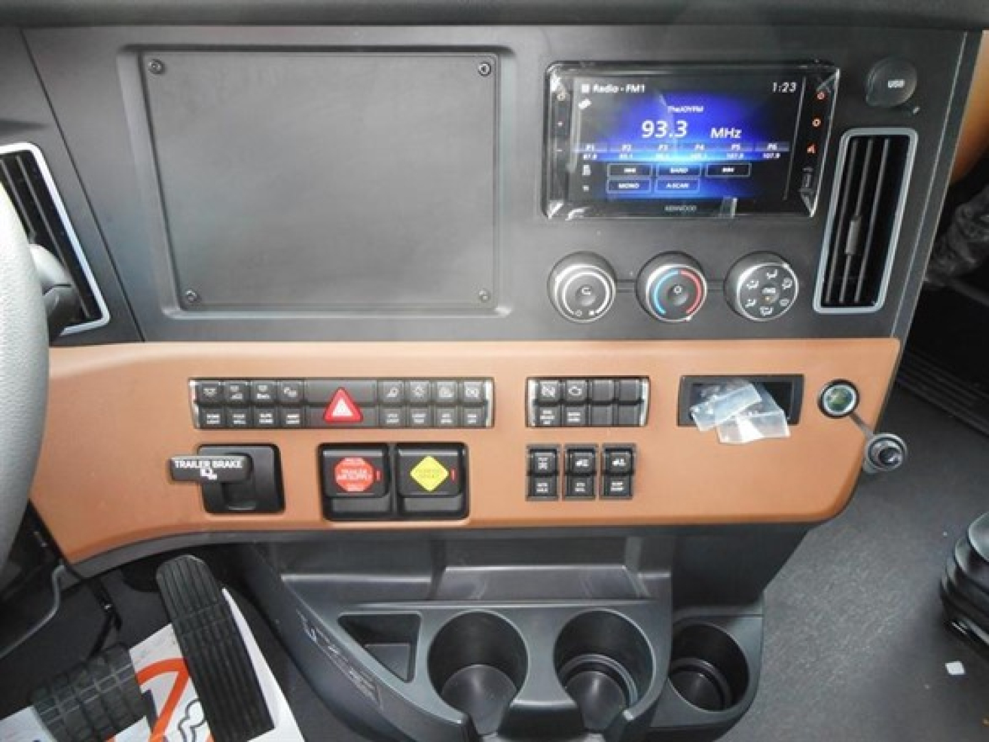 Dashboard interior of a Freightliner Cascadia cab showing a digital radio/display, climate controls, switches, and cup holders.