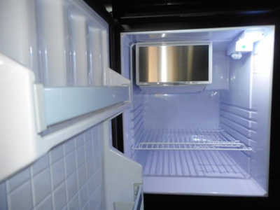 Fridge/freezer unit inside a Freightliner Cascadia cabin showing empty compartment with shelves and small monitor on back wall.