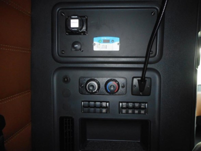 Truck cab interior panel with control knobs, vents, USB-like port, and a blue badge. Front overhead area shows a small square vent and circular knobs.