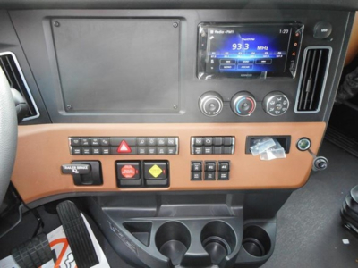 Dashboard interior of a Freightliner Cascadia cab showing a digital radio/display, climate controls, switches, and cup holders.