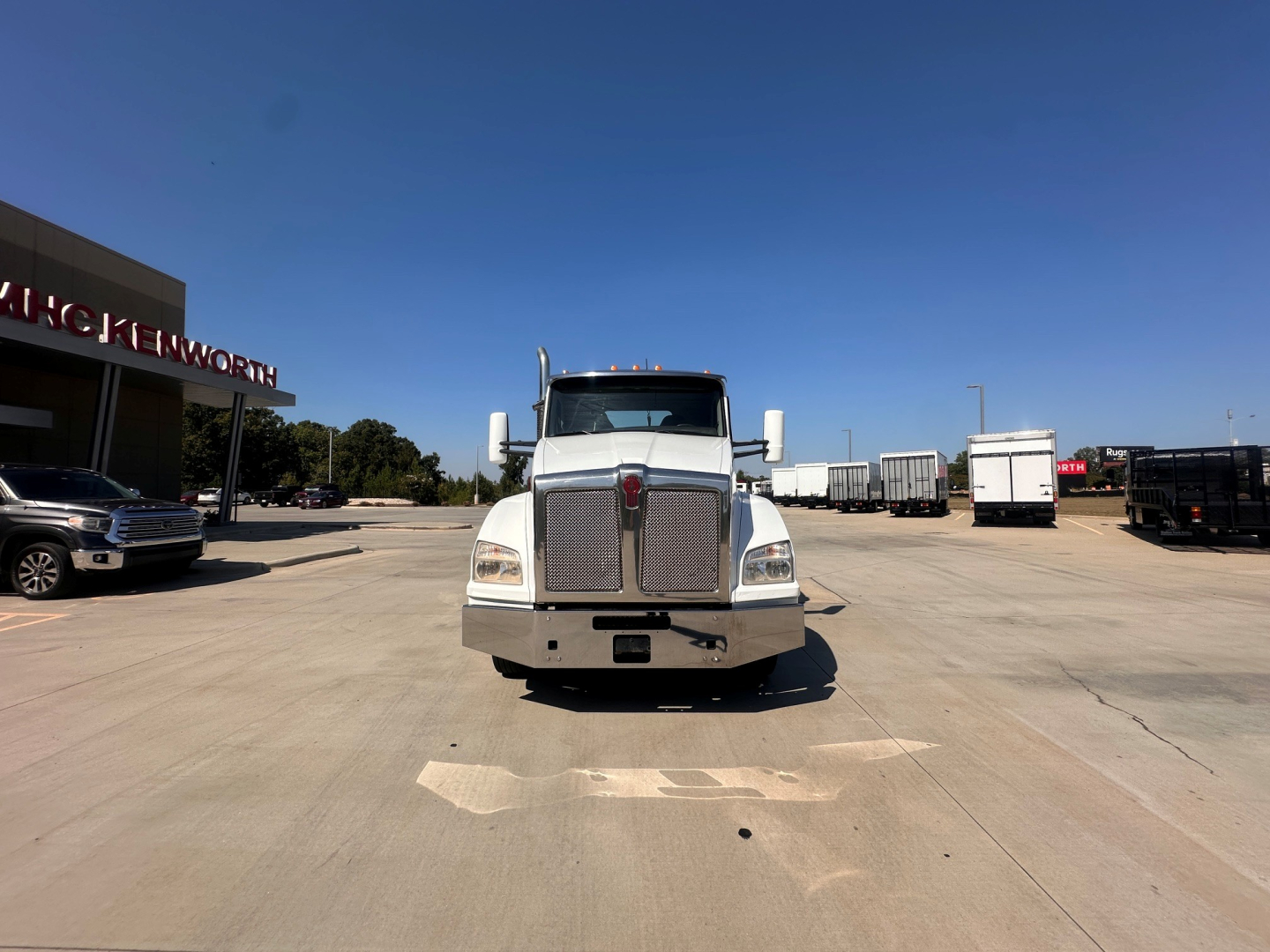 Kenworth T880 front view in a parking lot with grille, large bumper, and side mirrors.