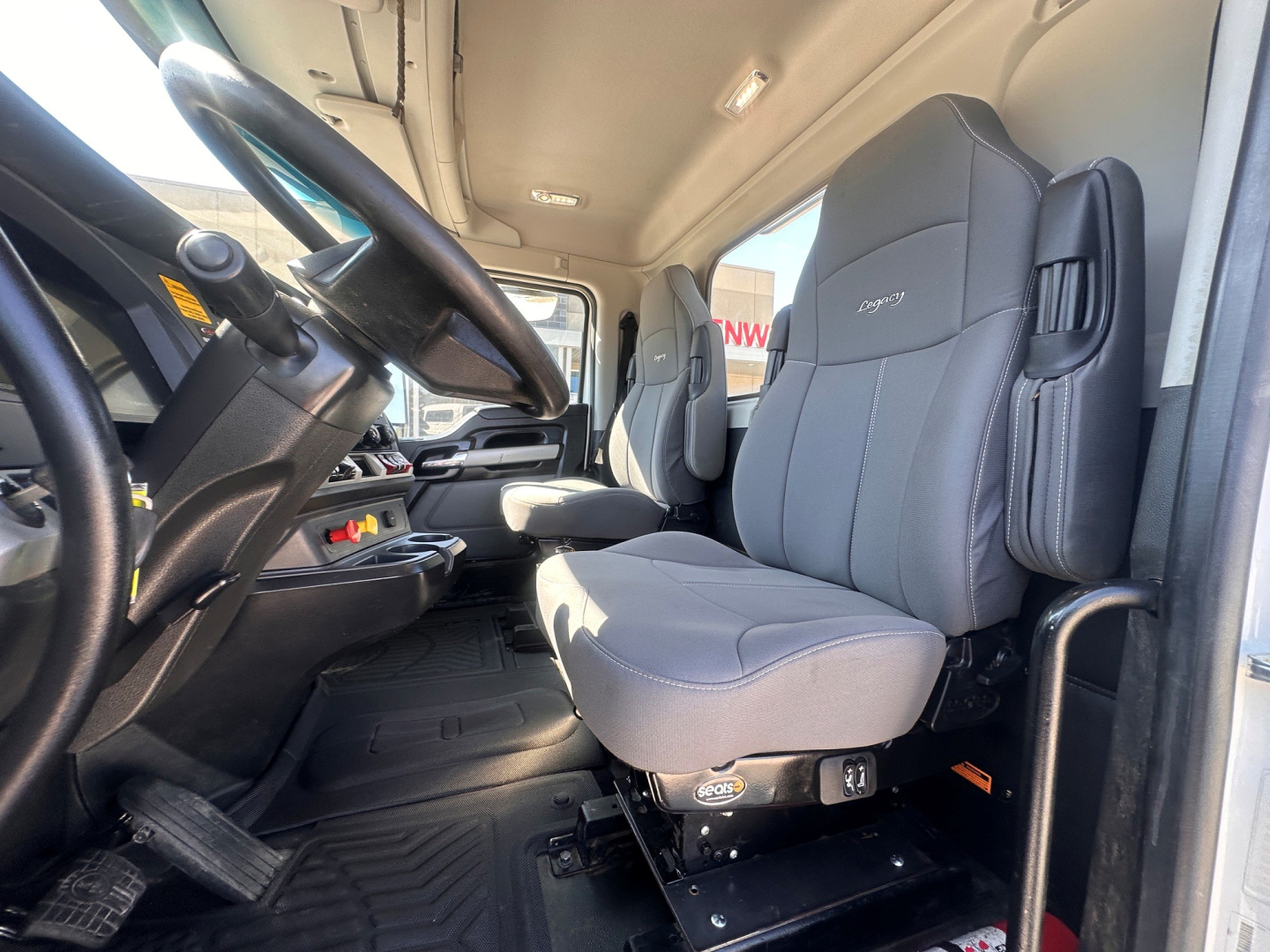 Kenworth T880 cab interior showing steering wheel, gray driver seat, and auxiliary seating with controls on seat base.