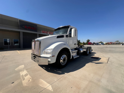 Kenworth T880 conventional day cab tractor in a dealership lot, side/front view, white cab with chrome grille, no trailer attached, clear sky.
