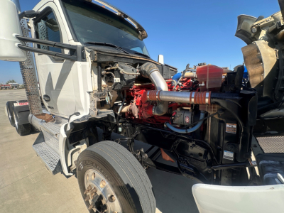 Kenworth T880 engine bay view showing red turbocharged diesel engine and surrounding components with front tire in foreground.