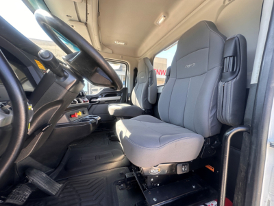 Kenworth T880 cab interior showing steering wheel, gray driver seat, and auxiliary seating with controls on seat base.