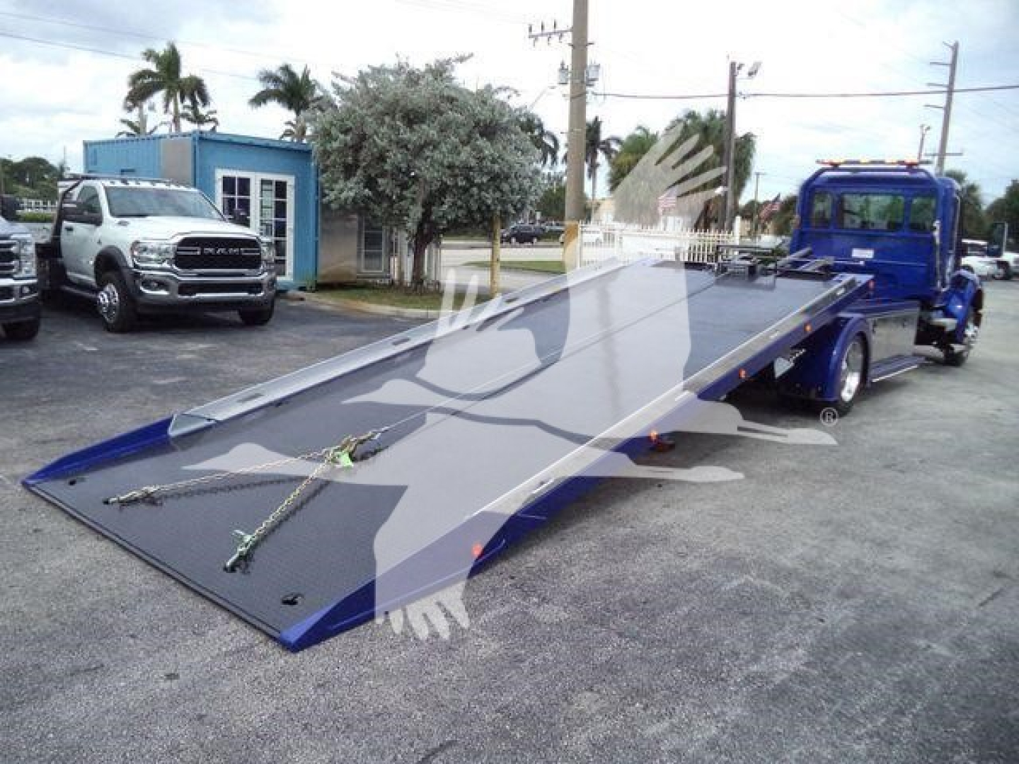 Tow truck rollback bed with Kenworth T280, blue hydraulic platform, and ramps visible in lot.