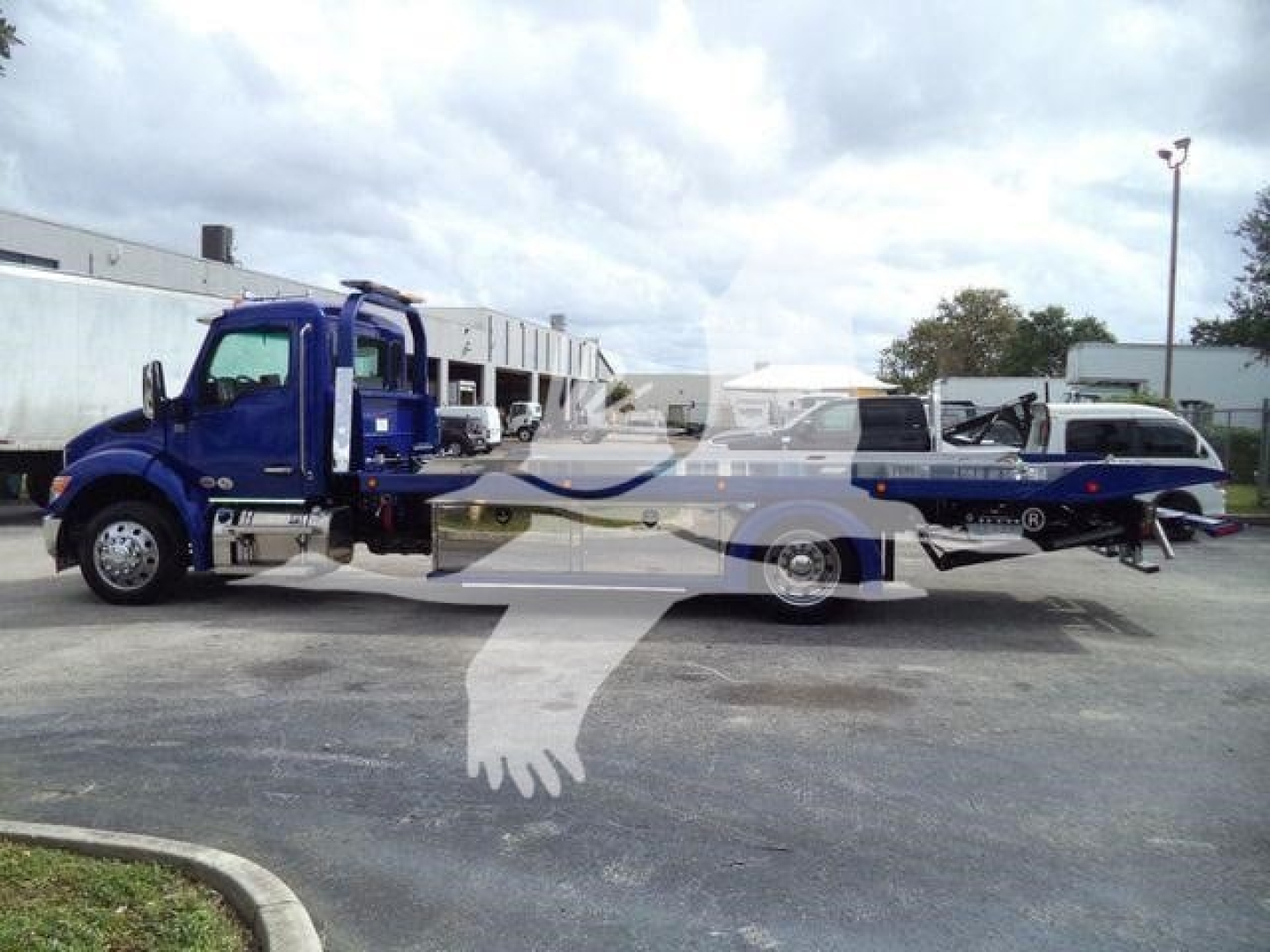 Truck with a rolled—back tow bed, blue chassis, and a flatbed tilt; side view shows Kenworth T280 style cab; no legible brand text visible in image