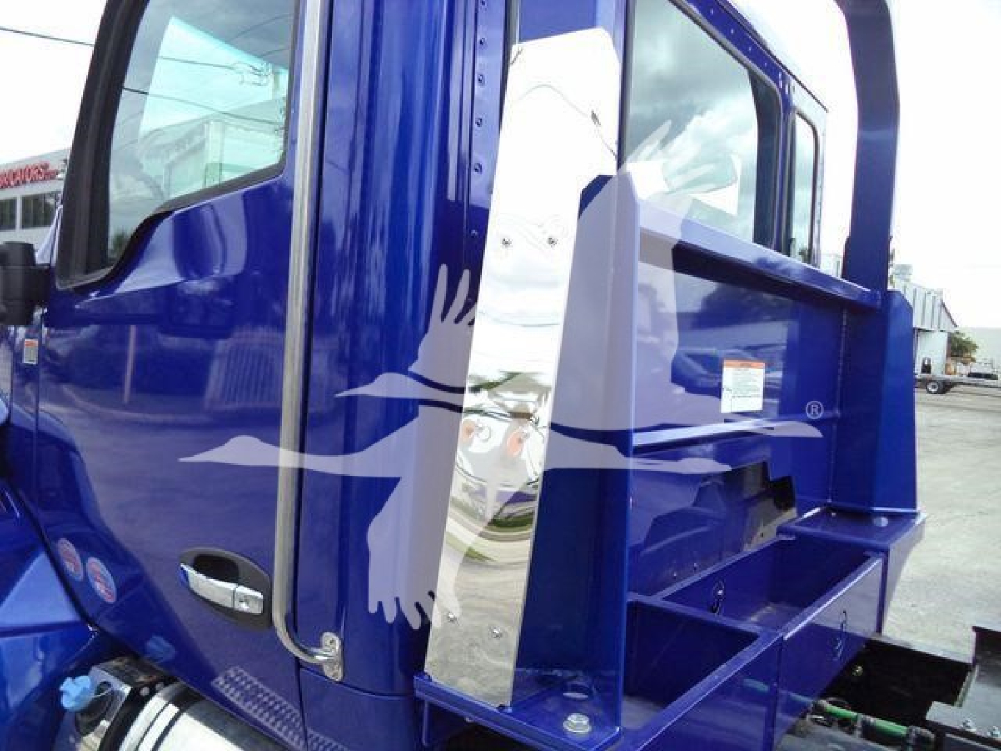 Truck cab side with blue paint and chrome handle, partial steps and decorative white graphic on door; Kenworth T680 or similar cab visible.