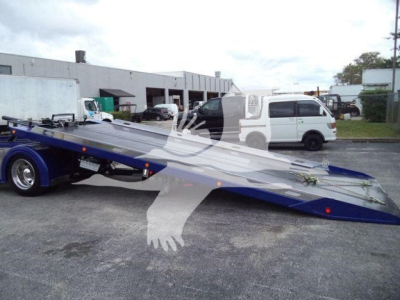 Kenworth T280 rollback wrecker trailer in a parking lot, blue platform with winch and ramps, white pickup in background, stock number KW2STEPSIDFM.