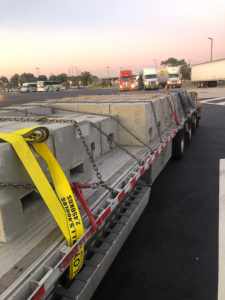 Flatbed trailer load deck showing blocks and chains securing cargo on a multi-axle trailer in a parking lot.