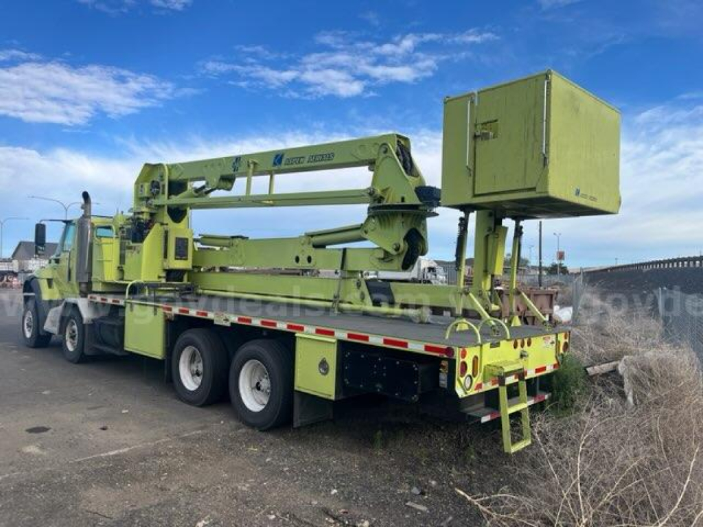 1500000-rpm International 7600 bucket truck with extendable boom on a flatbed trailer, green color, rear toolbox and guard rails visible.