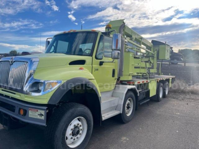 International 7600 bucket truck in serviceable condition with green boom and cab, front left view showing crane/bucket system and dual rear axles