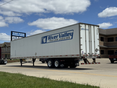 Trailer side view showing a River Valley Trailer Leasing logo on a white utility 4000D-X trailer with dual axles parked on a street.