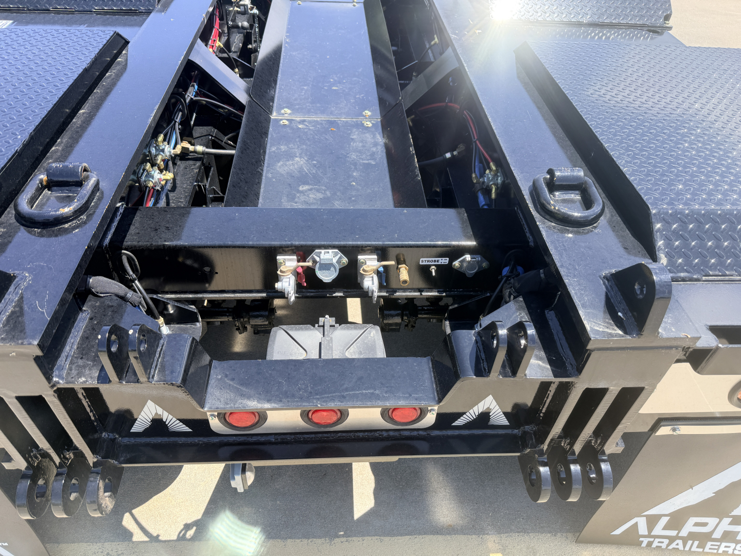 Trailer rear view showing coupling and hydraulic components on a lowboy trailer with XD insert and fresh paint; visible labels and mechanical fittings.