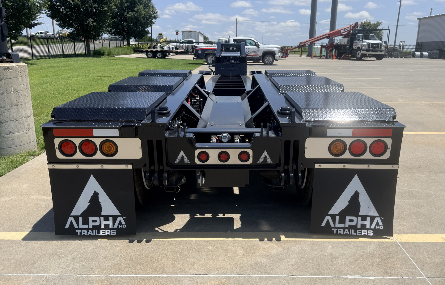 Alpha Trailers lowboy trailer rear view showing dual fenders with Alpha logos and diamond plate storage boxes on both sides.