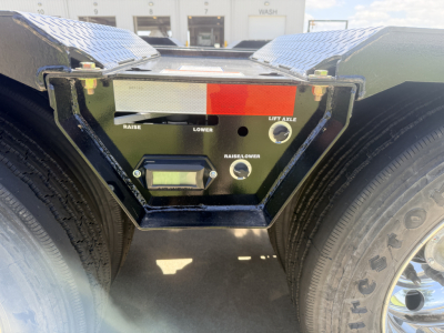 Trailer rear deck control panel showing raise/lower and lift axle controls with red/white gauge plate between dual axles.