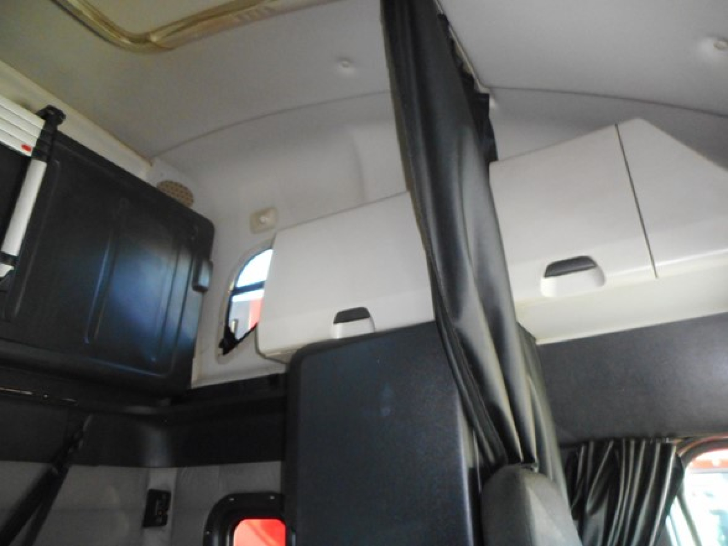 Truck cab interior showing sleeper compartment with cabinets and a partition, black and white color scheme, vertical curtains.