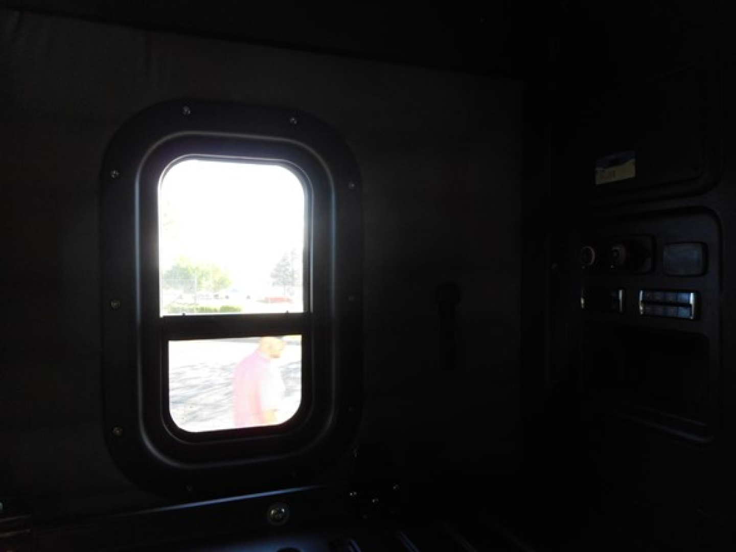Vehicle interior showing a small side window of a Freightliner Cascadia cab with a partial dashboard on the right.