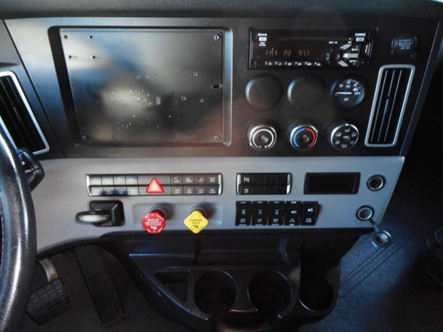 Freightliner Cascadia 126 dashboard view showing center console with hazard button, red/ yellow control knobs, cup holders, and panel area.