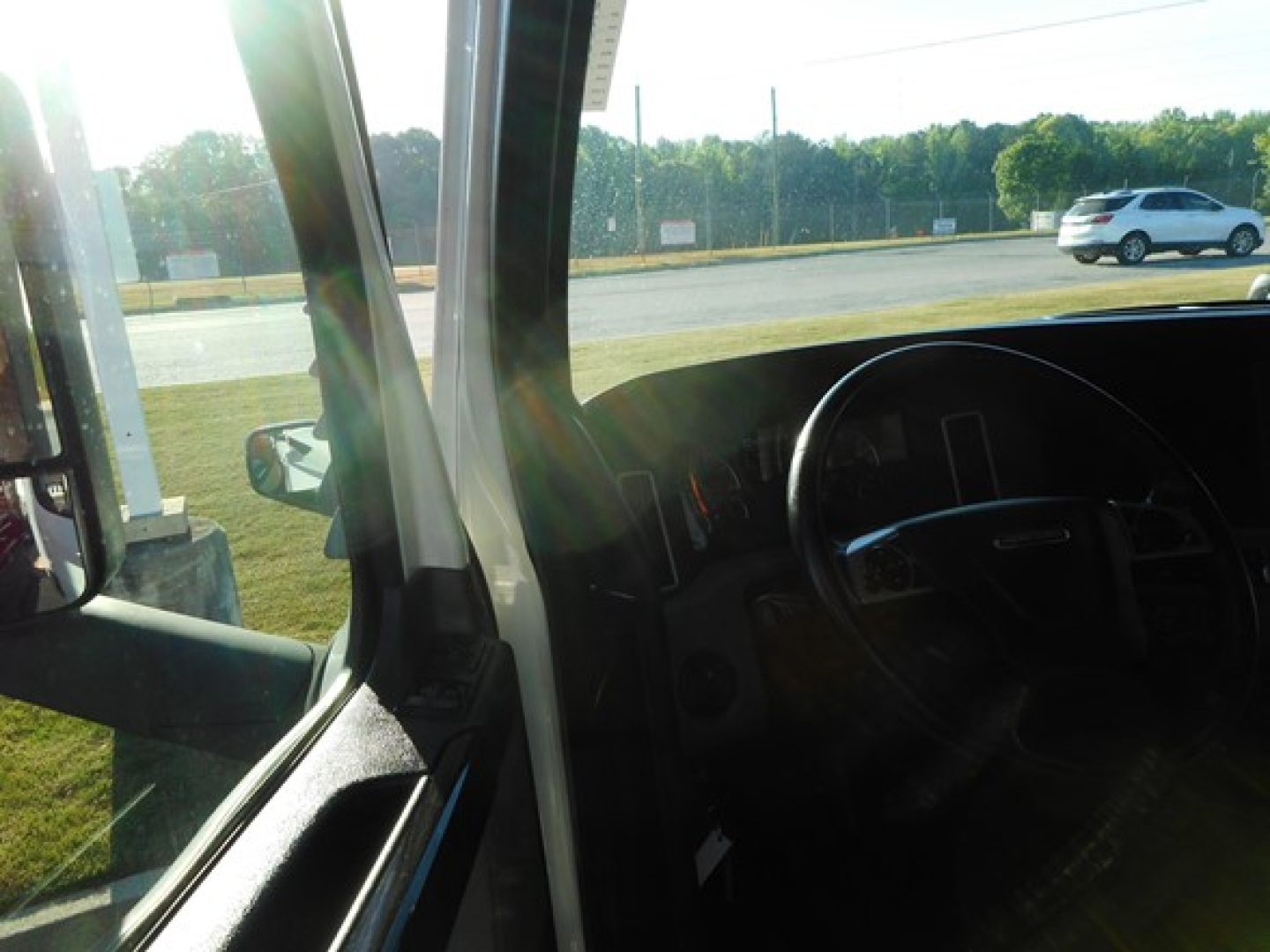 Freightliner Cascadia truck interior driver’s area with dashboard and steering wheel visible through the windshield, front door, and side mirror.