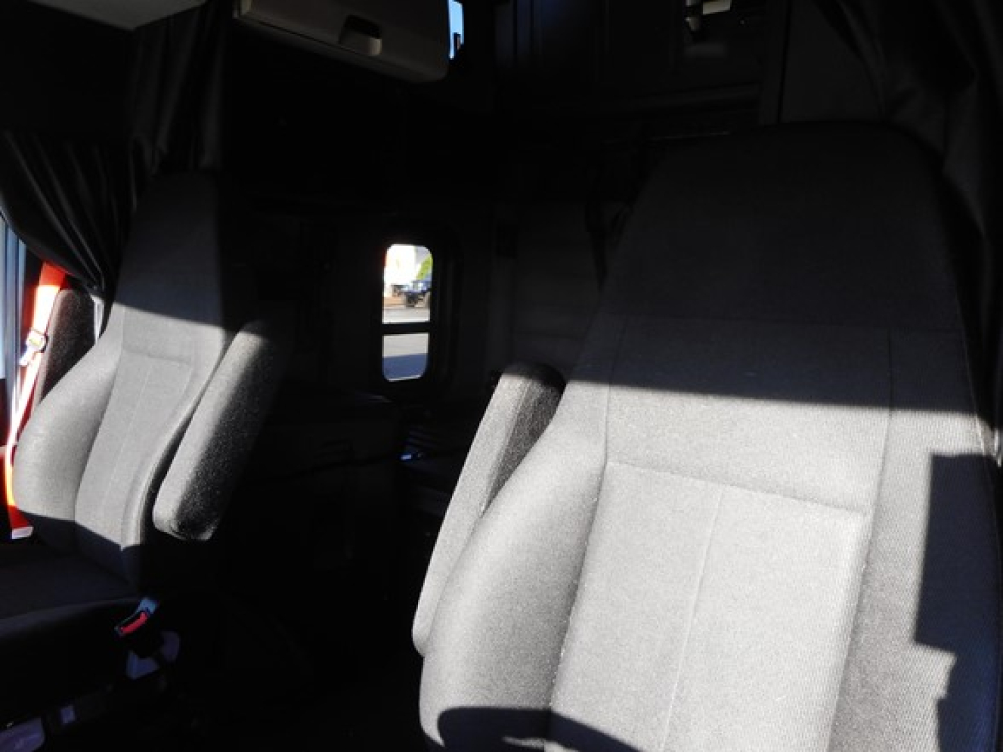 Cab interior of a Freightliner Cascadia showing front seats and sleeper area with windows and curtains.