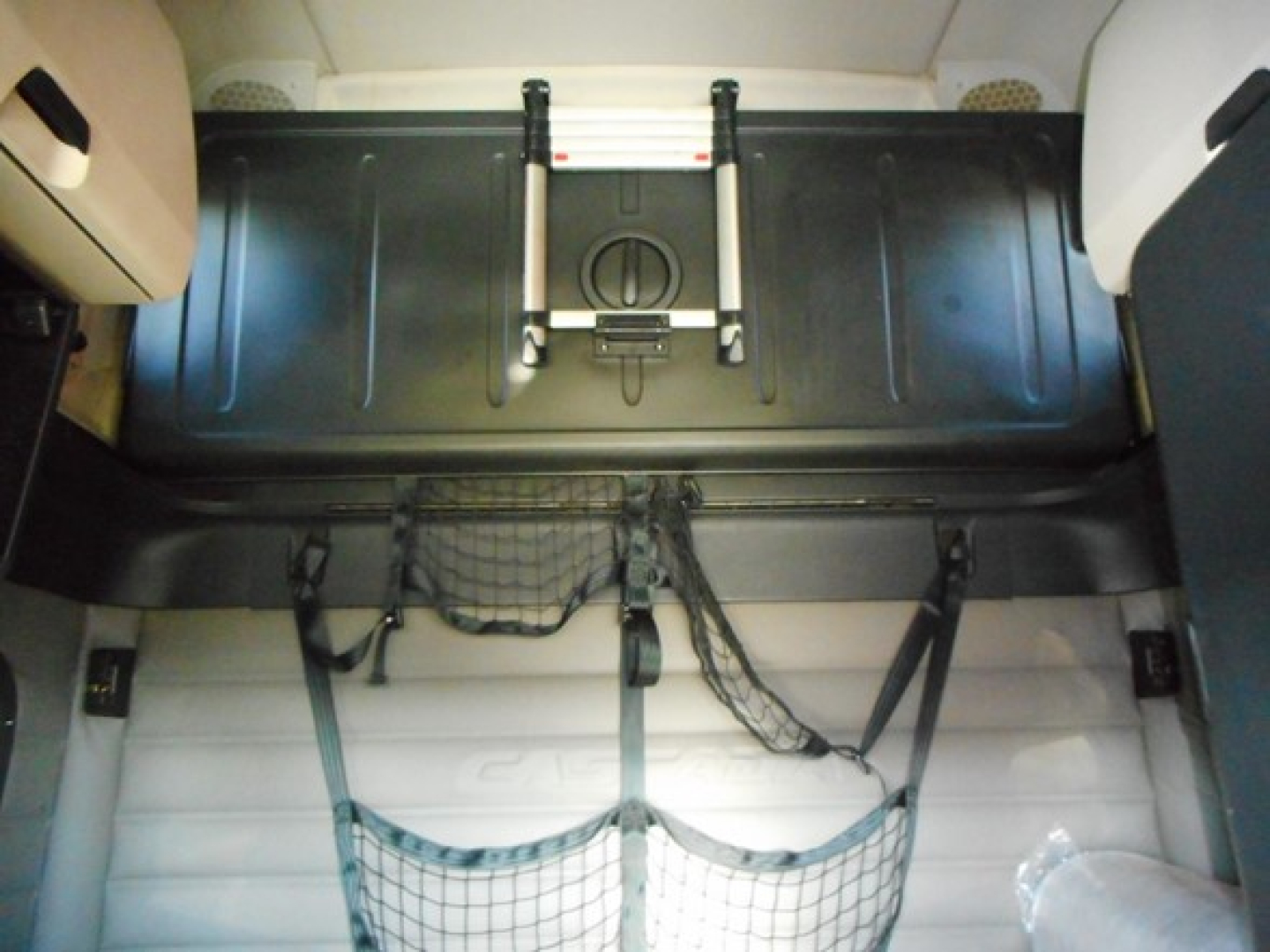 Freightliner Cascadia sleeper cab interior showing rear storage area with seat frame and cargo nets.