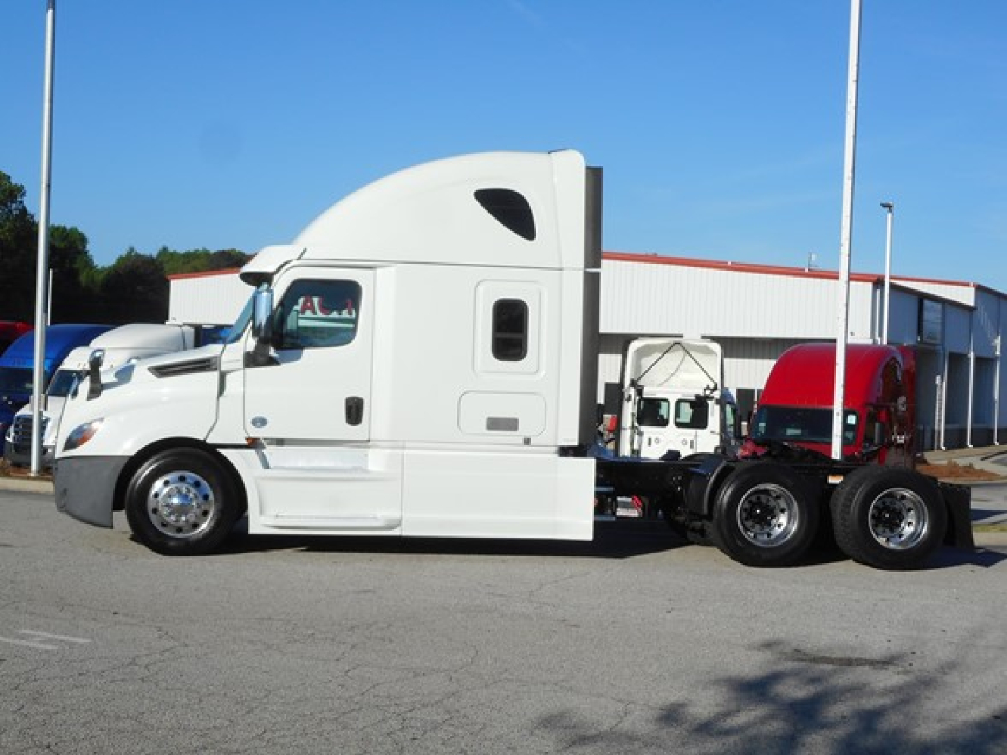 White Freightliner Cascadia 126 semi-truck tractor in a parking lot, long chassis with sleeper cab and dual rear axles.