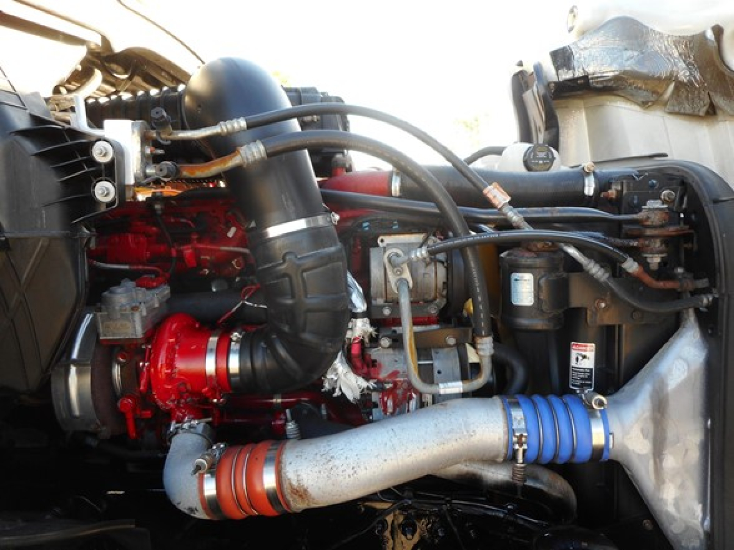 Truck engine bay showing red engine block, black hoses, and aluminum intake with blue silicone coupler in Freightliner Cascadia