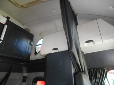 Truck cab interior showing sleeper compartment with cabinets and a partition, black and white color scheme, vertical curtains.