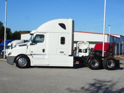 White Freightliner Cascadia 126 semi-truck tractor in a parking lot, long chassis with sleeper cab and dual rear axles.