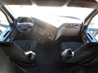 Truck cab interior view from driver seat showing steering wheel, dashboard, and center console with gauges and controls.