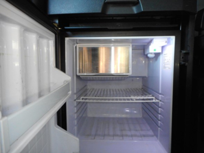 Fridge compartment of a Freightliner Cascadia sleeper truck showing empty freezer with small freezer chest and open door