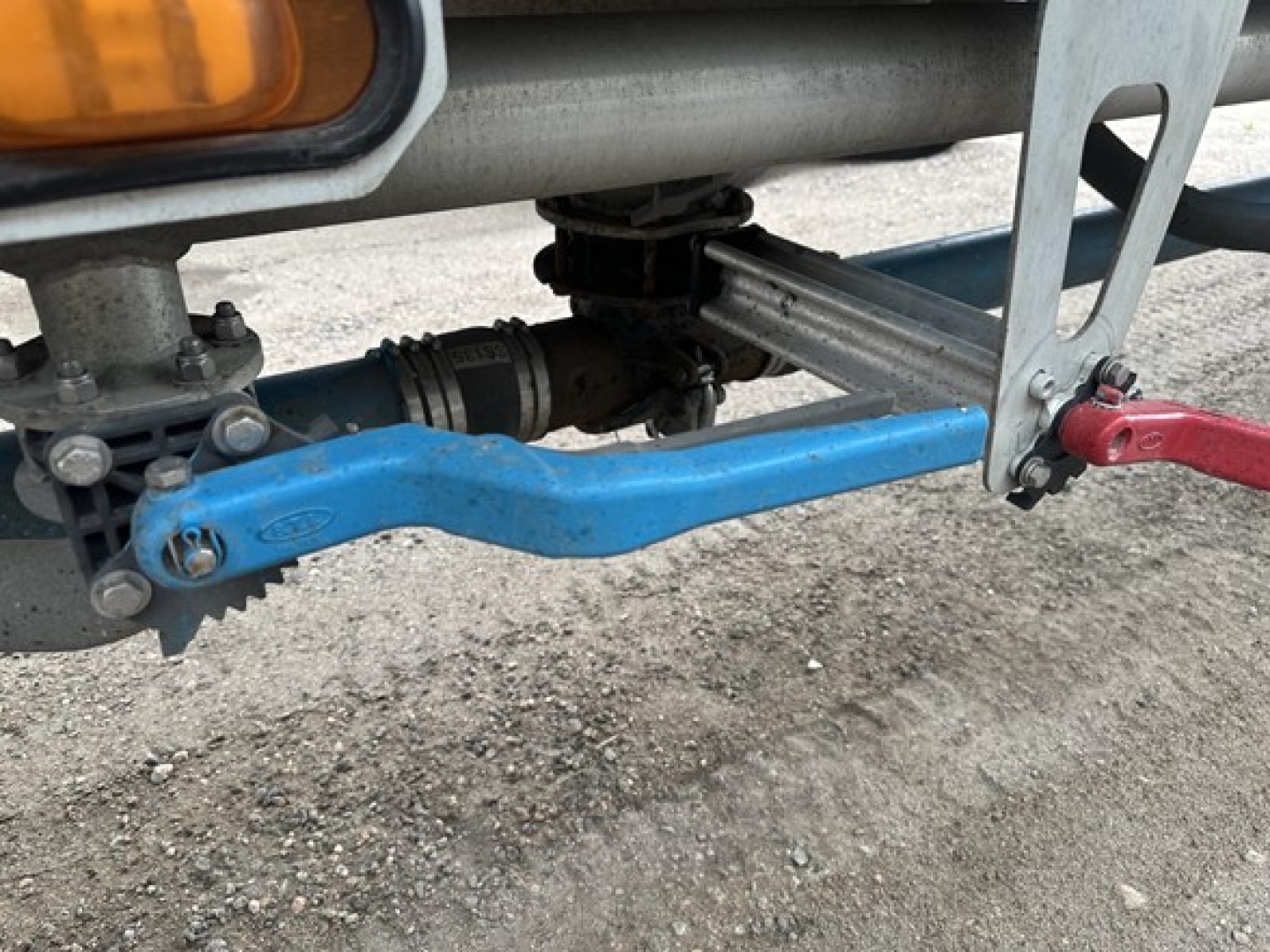 Trailer hitch and blue linkage visible under a 2019 Mac 1050 Cu Ft Pneumatic trailer showing rear suspension, pneumatic line, and mounting bracket.