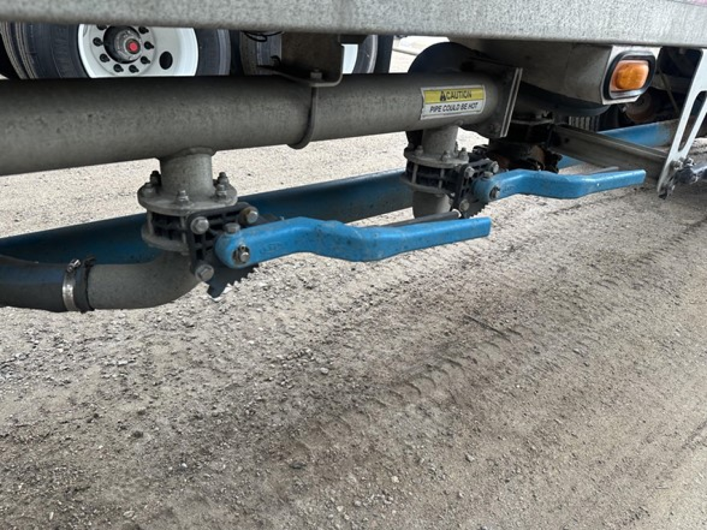 Trailer undercarriage showing blue spray-painted air/brake lines and axles with quick-connect fittings, pneumatic system components and a side warning sticker visible.