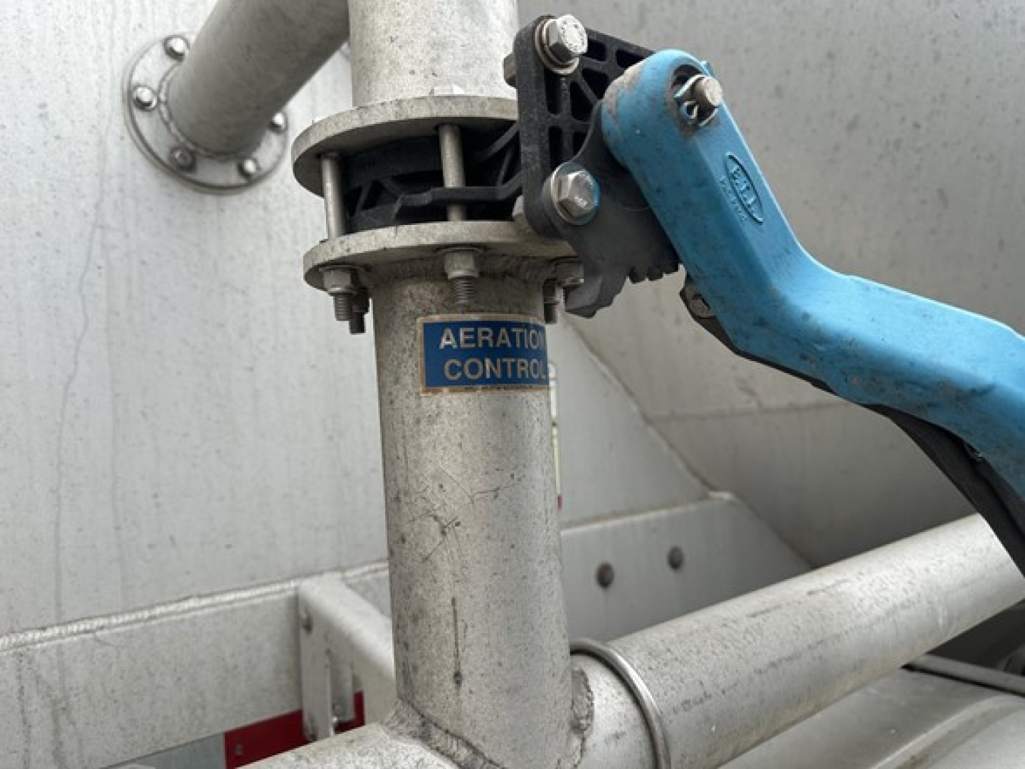 Pneumatic trailer component showing aeration control valve on a vertical cylindrical chute with blue lever in foreground.