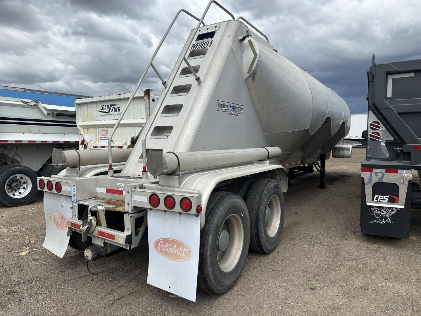 Semi-trailer tanker with three-axle rear, pneumatic dry bulk trailer, white/gray, rear view showing rear bumper, taillights, mud flaps, and ladder with 'Mac' branding.