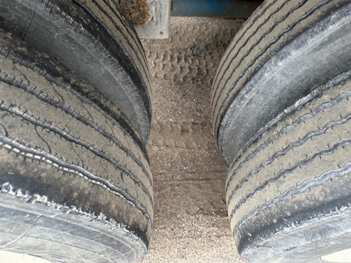 Dual rear pneumatic trailer tires mounted on a Mac 1050 cu ft pneumatic trailer showing tread wear and dirt between wheels.