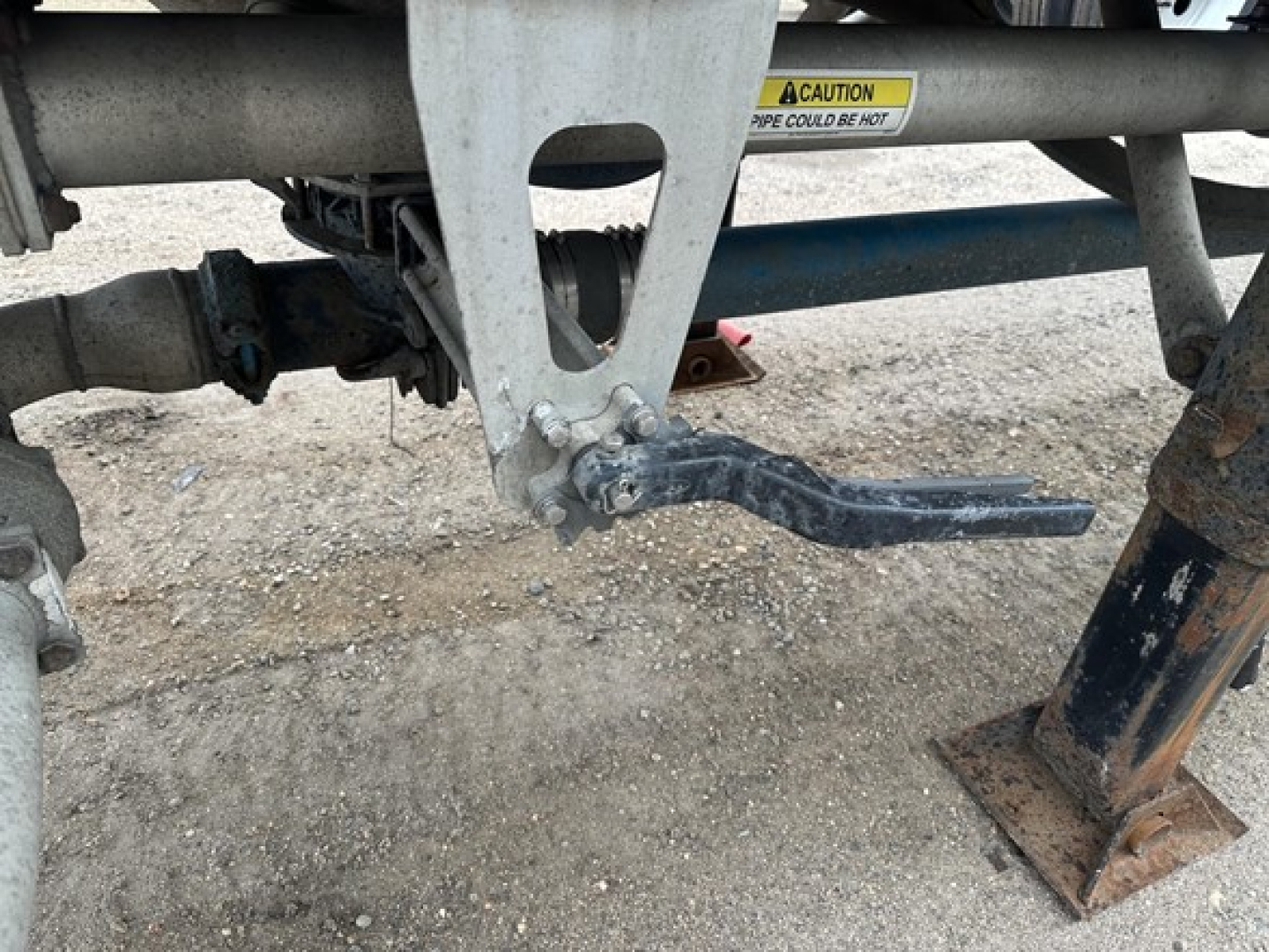 Trailer leaf spring and suspension components visible under a Pneumatic dry bulk trailer with caution sticker and metal frame text.