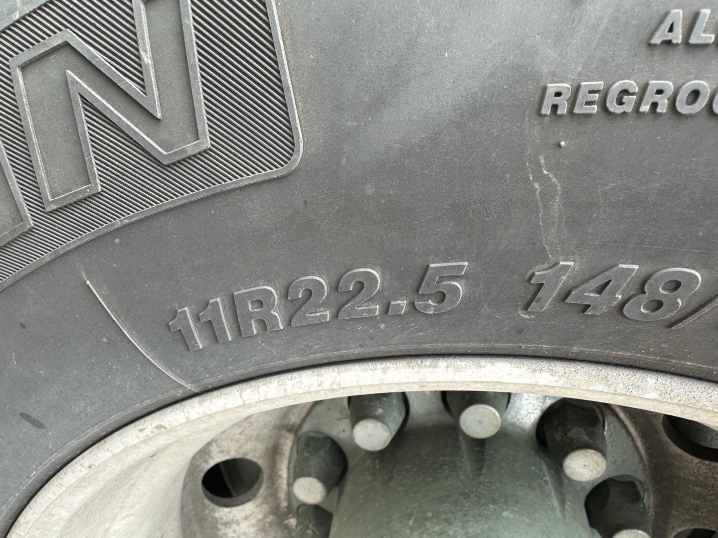 Trailer wheel and tire with visible tread and embossed markings including 11R22.5 148; aluminum wheel; pneumatic dry bulk trailer edge.
