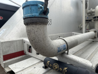 Pneumatic dry bulk trailer showing a curved exhaust/pipe with blue valve and metal framework; label and hoses visible.