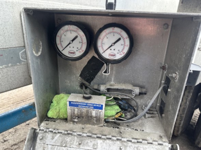 Gauge panel showing two round pressure gauges with a metal enclosure and a label reading suspension load scale INTAK 250 inside a pneumatic trailer dash area.