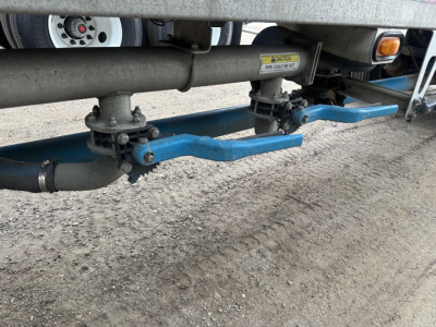 Trailer underside showing blue support arms and pneumatic hoppers assembly with warning labels; appears to be a Mac 1050 cu ft pneumatic trailer with air ride rear suspension.