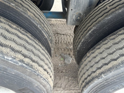 Mac 1050 pneumatic trailer wheel dual tires with tread and salt dirt. View of tandems and frame showing wheel hubs.