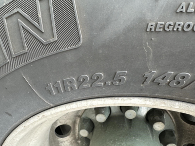 Trailer wheel and tire with visible tread and embossed markings including 11R22.5 148; aluminum wheel; pneumatic dry bulk trailer edge.
