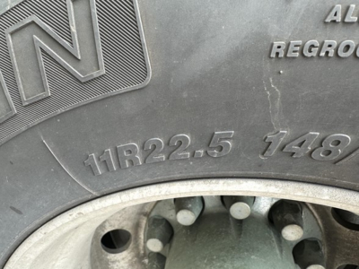 Tire sidewall with raised markings 11R22.5 148 and N logo visible, wheel hub area and valve stem in view.