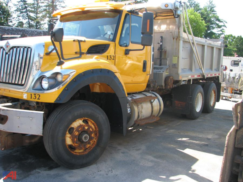 Vehicle side view of a yellow 2015 International WorkStar 7600 dump truck with front dual tires, visible wheel with rusted rim, and dump bed