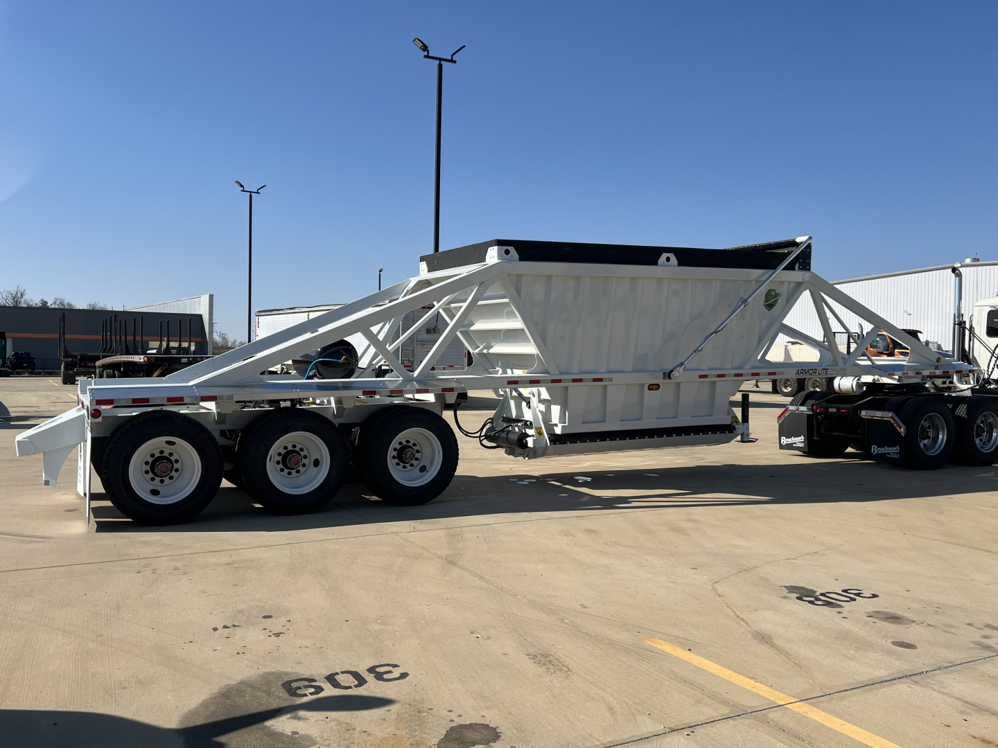 Wheel-end view of a white Armor Lite SBD42 tri-axle air ride trailer with a dump bed, exposed chassis, and multiple axles.