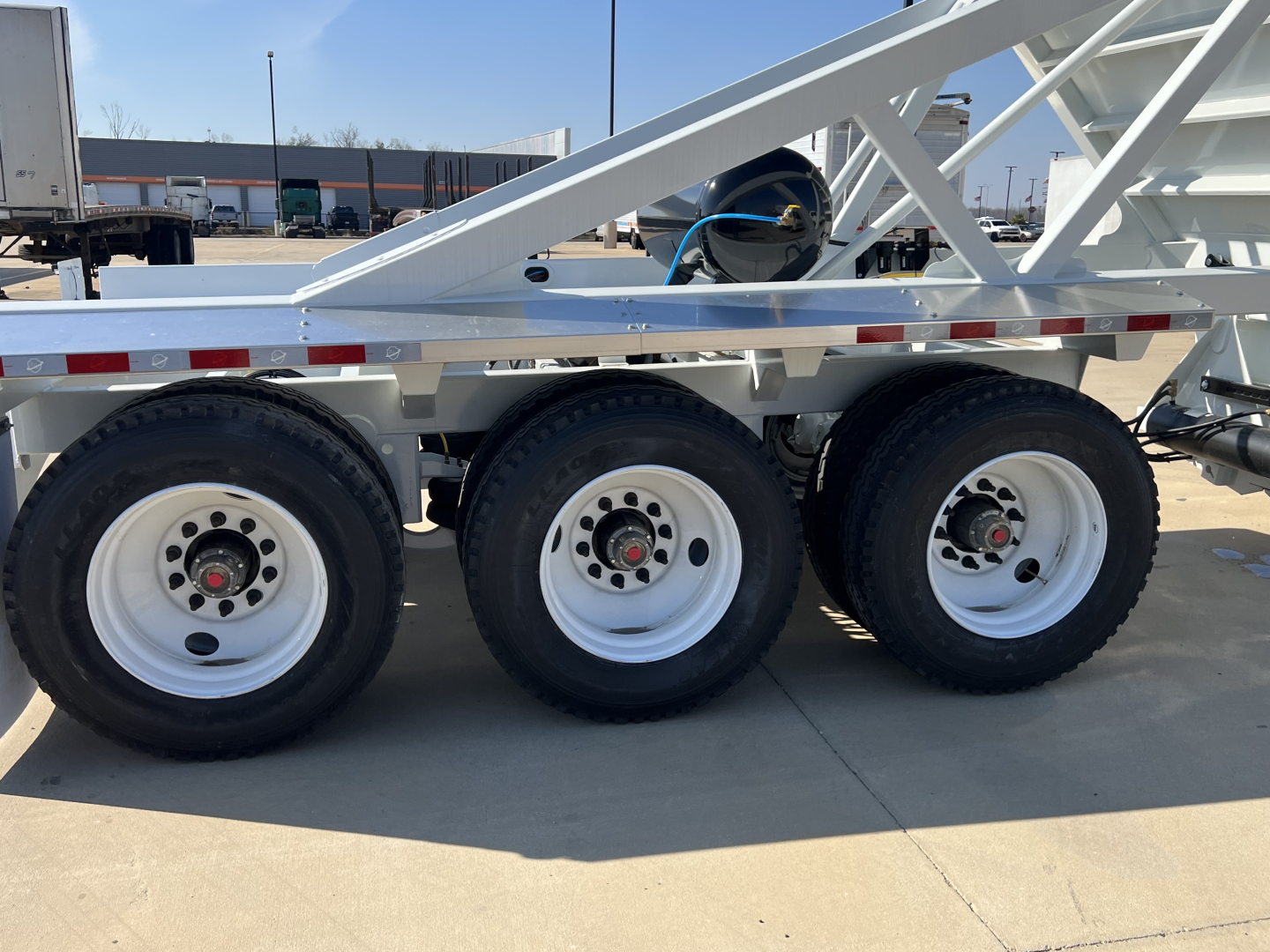 Three axles with large white rims and tires under a white dump trailer frame