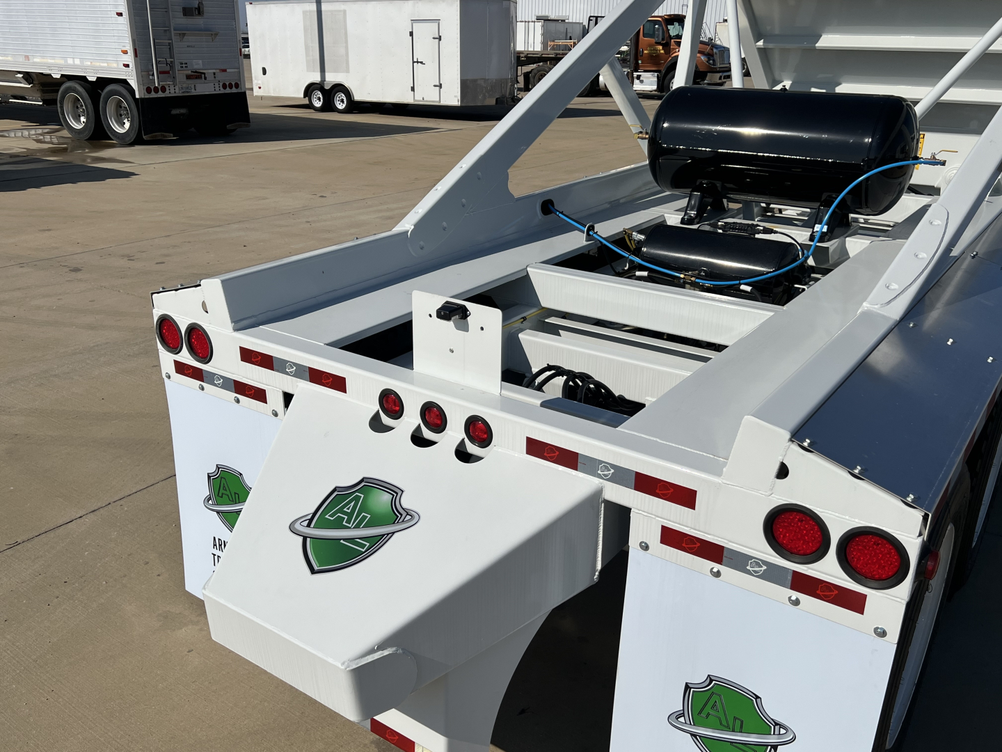 Dump trailer rear view showing white Armor Lite SBD42 tri-axle air ride suspension, rear lights, and green emblem patches on each mud flap.